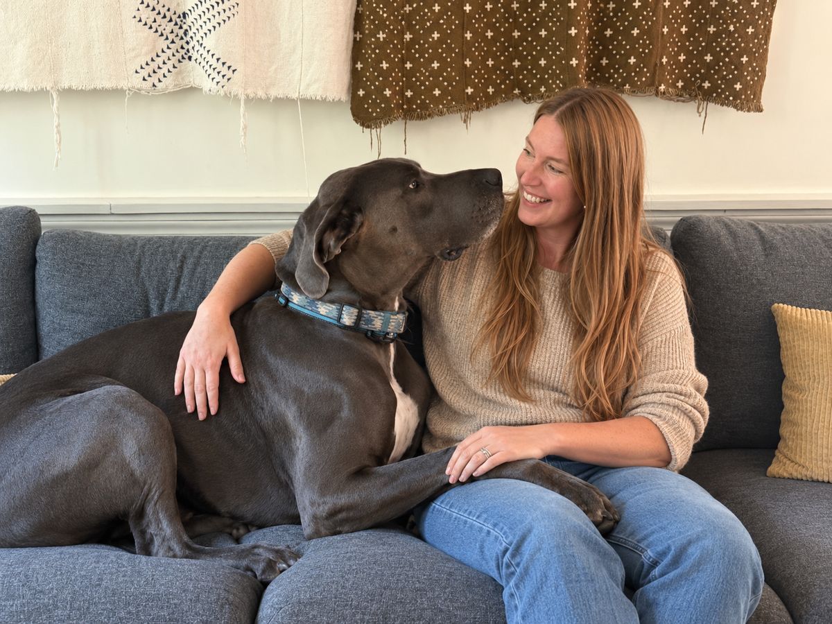 Susie on the couch at home with Zeus, her Great Dane, the two of them looking at each other and Susie laughing.